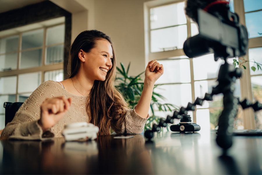 Chica sonriente grabando vídeo con un trípode mientras sonríe a la cámara
